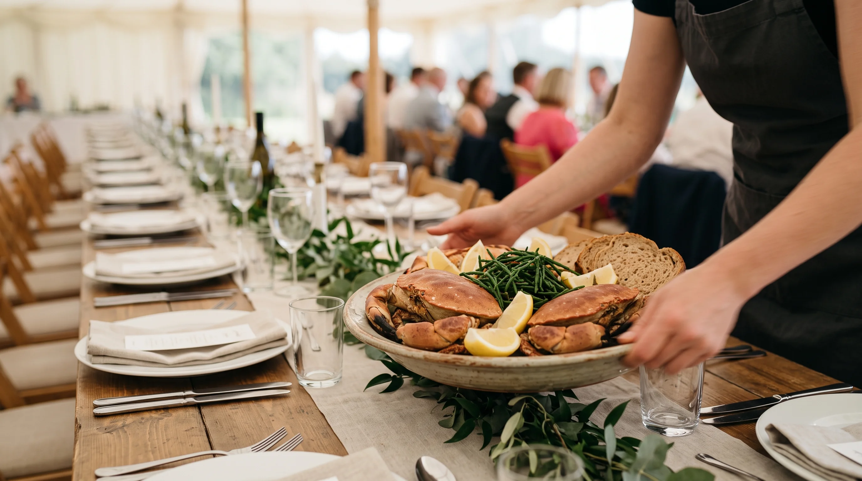 A wide platter of dressed Cromer crab being set down between guests along a long wedding table in daylight